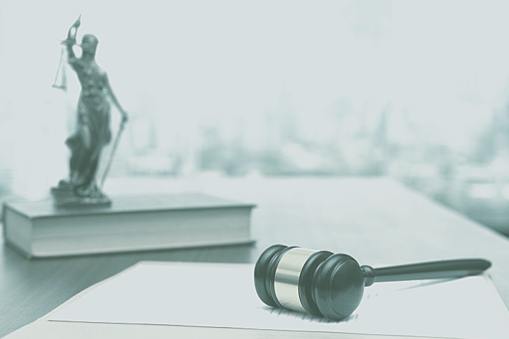 [ai] A wooden gavel lies on a stack of legal documents, with a statue of Lady Justice in the background, symbolizing law and justice in a professional legal setting.